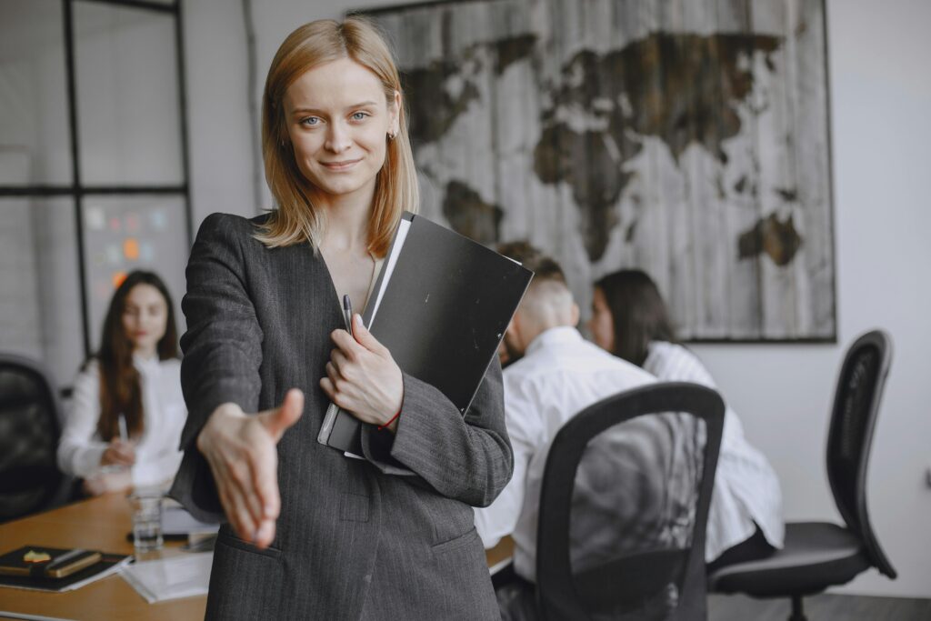 Professional woman offering a handshake in a vibrant office setting, symbolizing teamwork and collaboration.